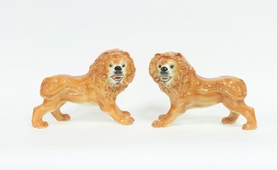 Lot 153 - A pair of pottery standing lions, with glass...