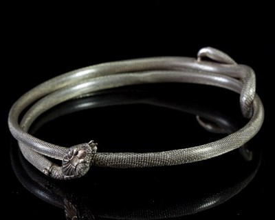 Lot 485 - A coiled snake bangle, the textured head with...