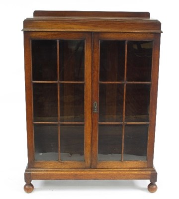 Lot 696 - A 1930s oak glazed display cabinet on ball...