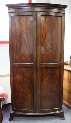 Lot 992 - A mahogany bowfront wardrobe, enclosed by twin-...