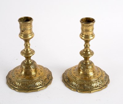 Lot 419 - A pair of engraved brass candlesticks on skirt...