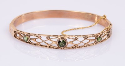 Lot 61 - A hinged bangle set with three peridot in a...